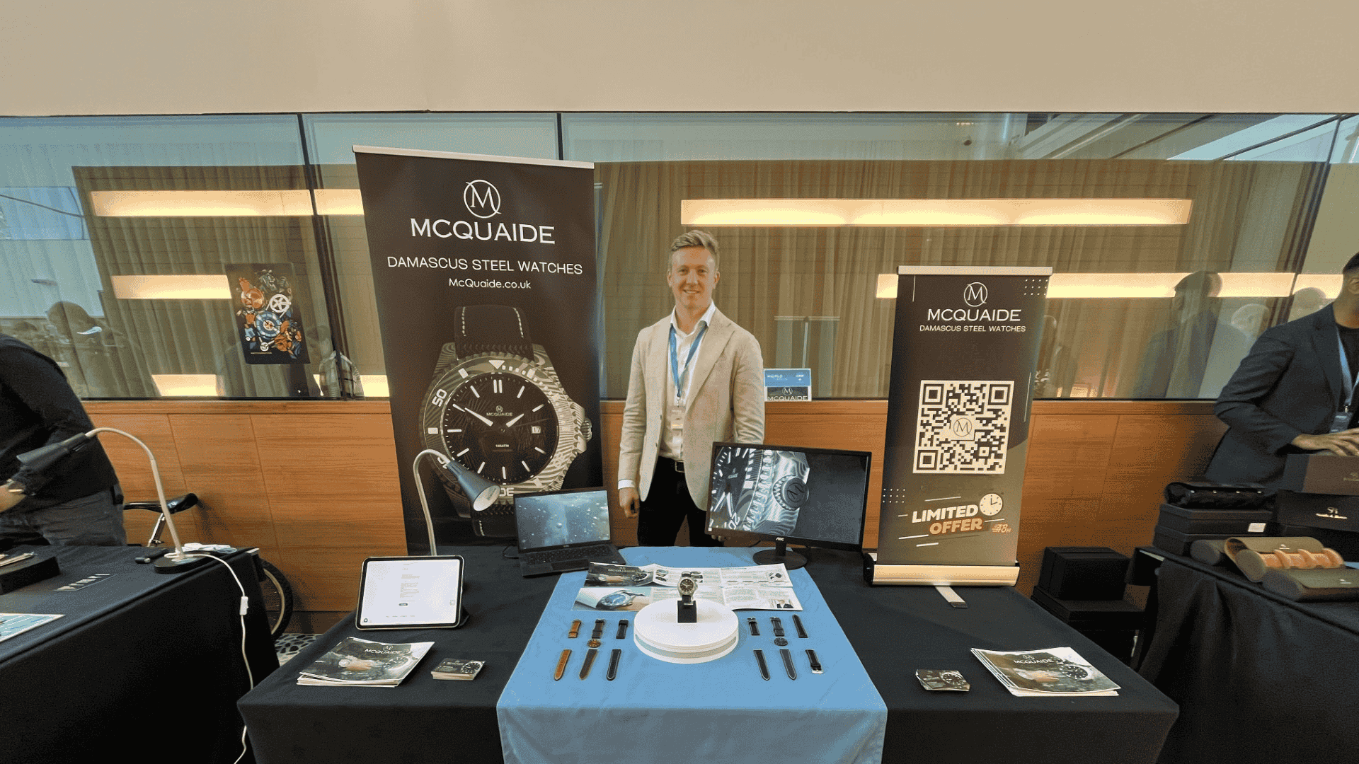Person standing behind a table with a McQuaide watch display at an event.