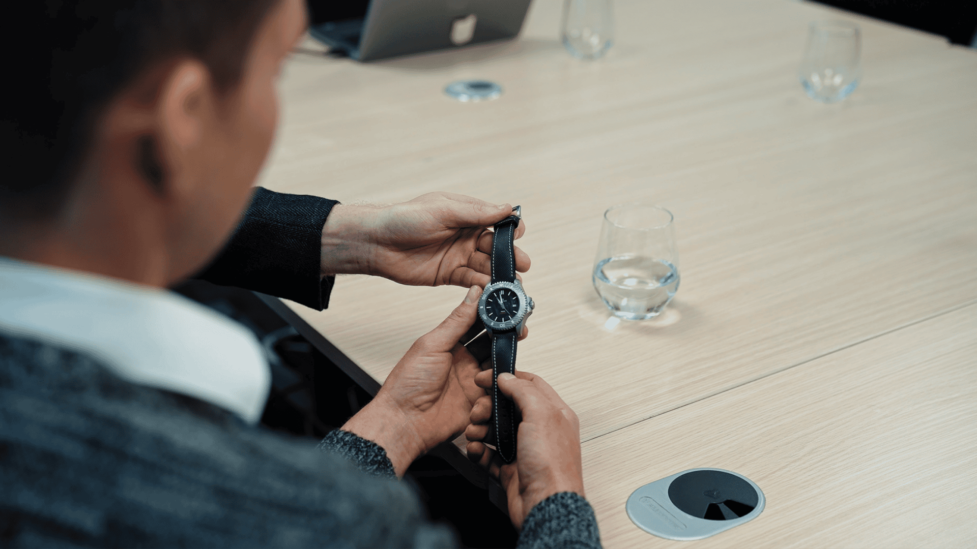 Person adjusting a Damascus Steel watch in an office setting with a glass of water on a table.